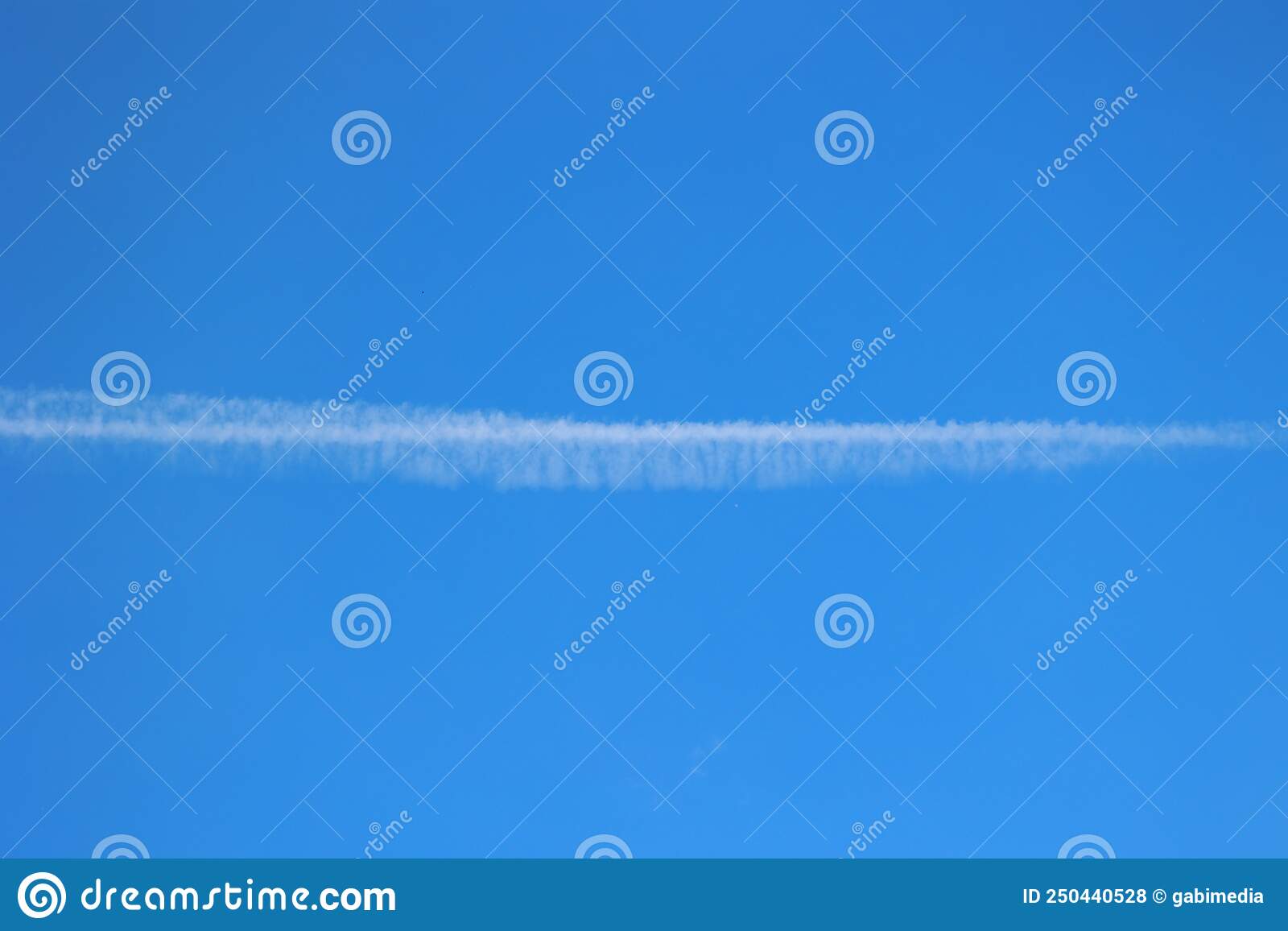 Nice day with blue sky and a cloud made by the engine of an airplane